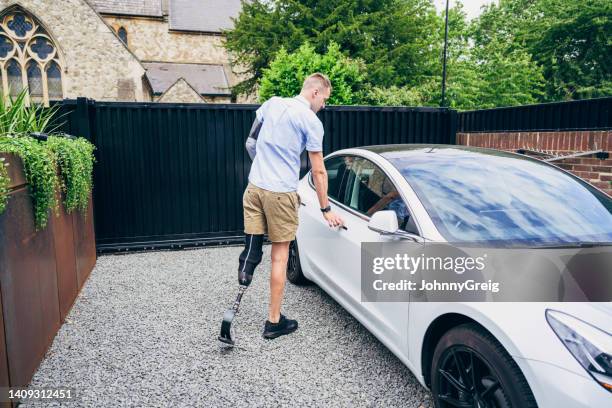 man with prosthetic arm and leg getting into electric car - car on driveway bildbanksfoton och bilder