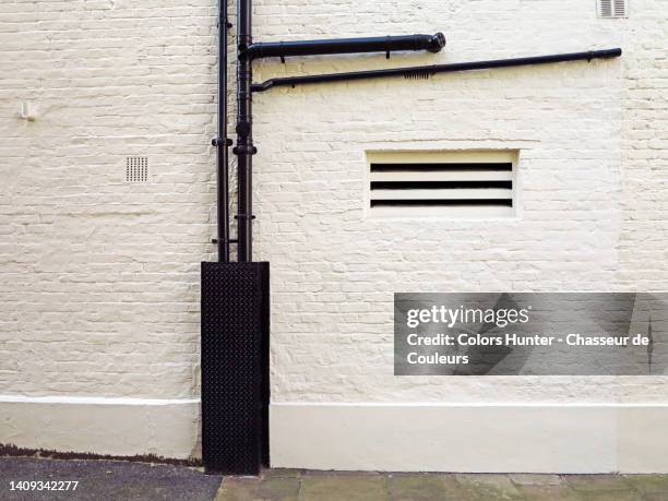 white brick wall with black metal water pipes and sidewalk in london, england, uk - verwittert stock-fotos und bilder