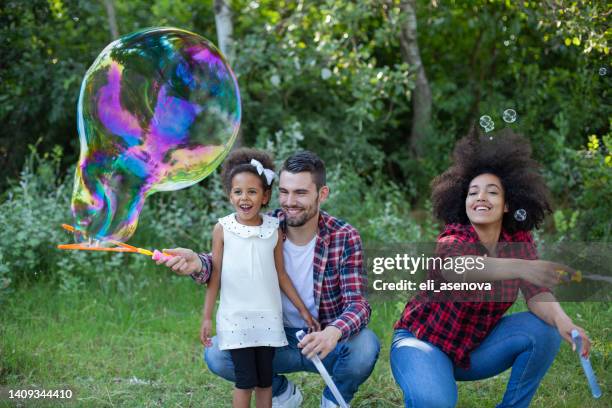 happy family playing soap bubbles in park - bubbles happy stockfoto's en -beelden