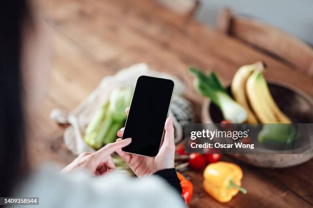 over the shoulder shot of young woman using smart phone after coming home from grocery shopping - shopping list stock pictures, royalty-free photos & images