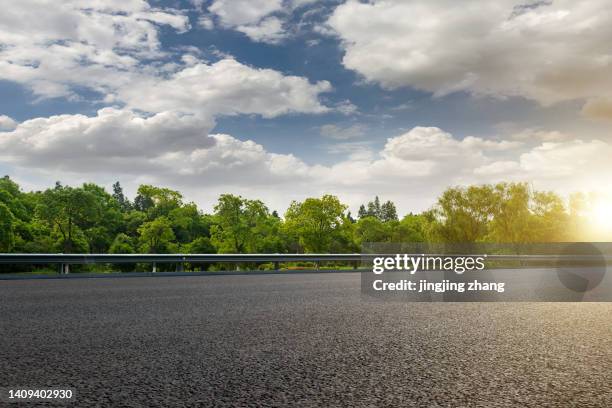 asphalt highway passing by the edge of dense woods on clear sky with dense white clouds - tejer stock-fotos und bilder