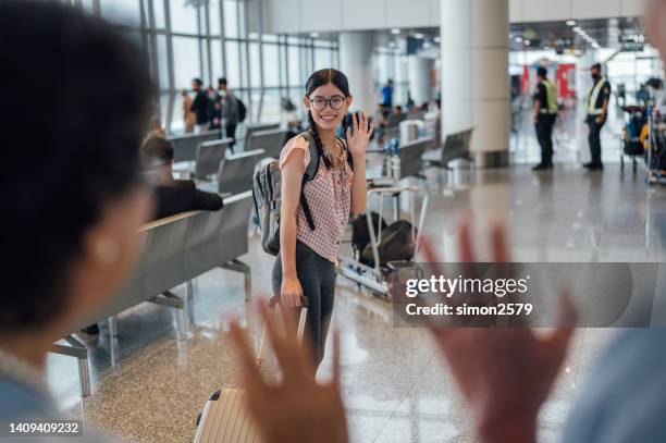 young asian girl waving hand for greeting to her parent at airport boarding gates - leaving stockfoto's en -beelden