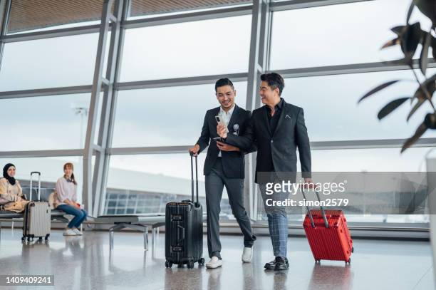photo de deux hommes d’affaires chinois d’origine asiatique marchant avec des bagages à l’intérieur du terminal de l’aéroport. - asian businessman phone photos et images de collection