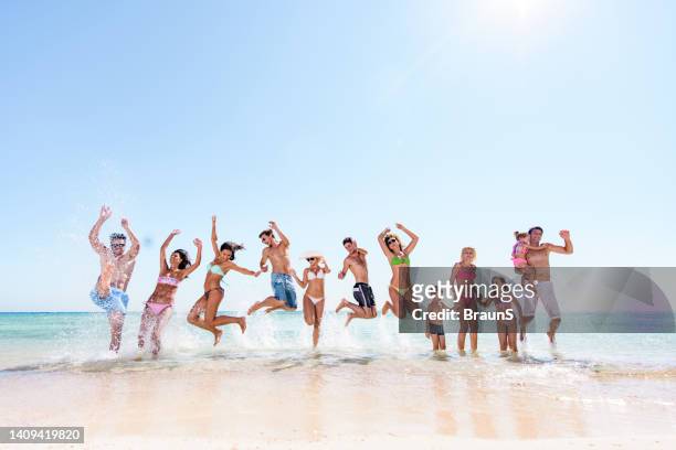 large group of carefree people jumping in summer day on the beach. - beach family jumping stock pictures, royalty-free photos & images