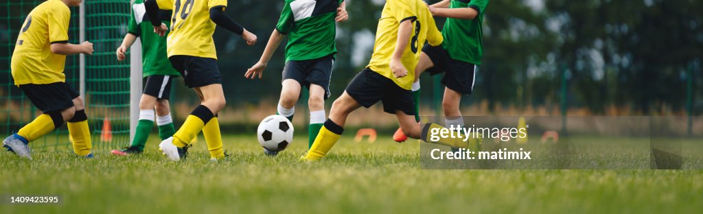 Kids play football on outdoor field. Children score a goal during a soccer game. Boys kicking ball. Running children in team jersey and cleats. School football club. Sports training for a young player