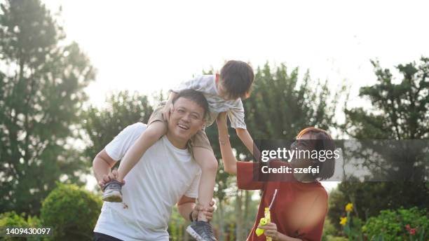 young boy riding on his father's shoulders at outdoor park, asian family. - putrajaya imagens e fotografias de stock