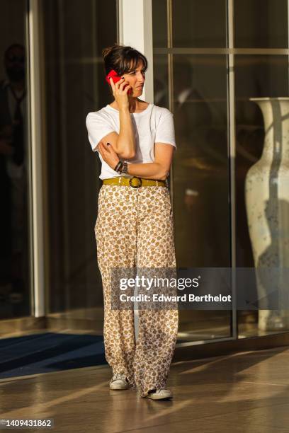 Guest wears a white t-shirt, a yellow mustard leather belt, beige and brown print pattern large pants, a black shiny leather Happy bracelet from...