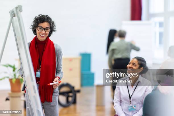 reife geschäftsfrau bei der präsentation auf flipchart vor kollegen in der werkstatt - flipchart stock-fotos und bilder