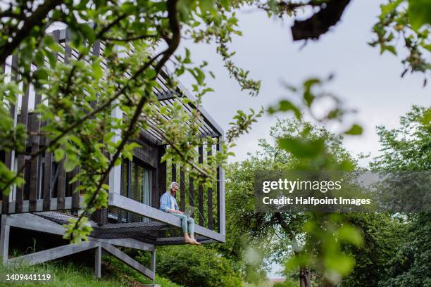 man with laptop and headphones working outside in tree house. - bâtiment écologique photos et images de collection
