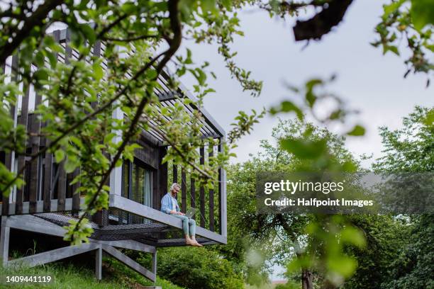 man with laptop and headphones working outside in tree house. - eco house ストックフォトと画像
