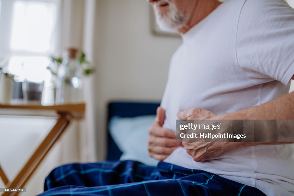 Senior man with stomach pain sitting in bed.