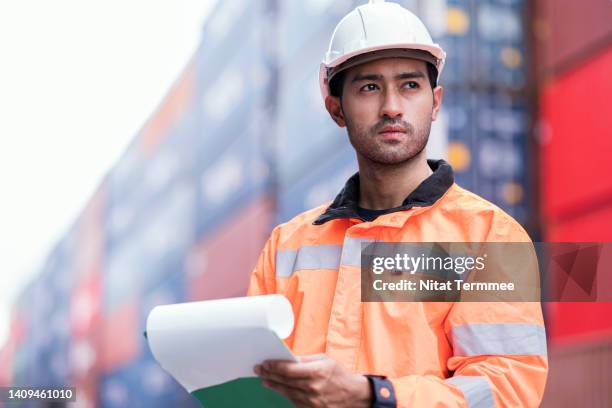 low angle view of commercial dock engineer holding shipment checklist at cargo container yard. supply chain and logistic, global business, freight forwarder business - casco de trabajo fotografías e imágenes de stock