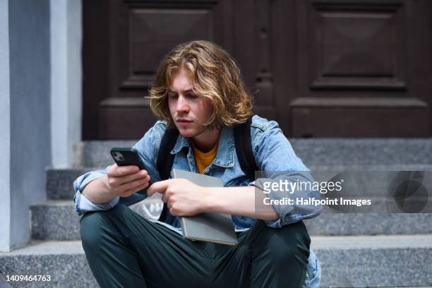 student boy sitting at school staircase, using smartphone. - online bullying foto e immagini stock