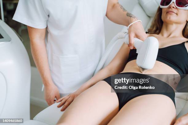 woman in protect eyeglasses and bikini lying on a couch, getting laser hair removal procedure for belly - ausbeutung stock-fotos und bilder