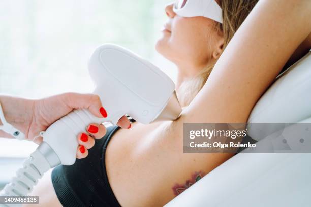woman in protect eyeglasses lying on a white couch getting armpit laser hair removal procedure. no more razor - laser stockfoto's en -beelden