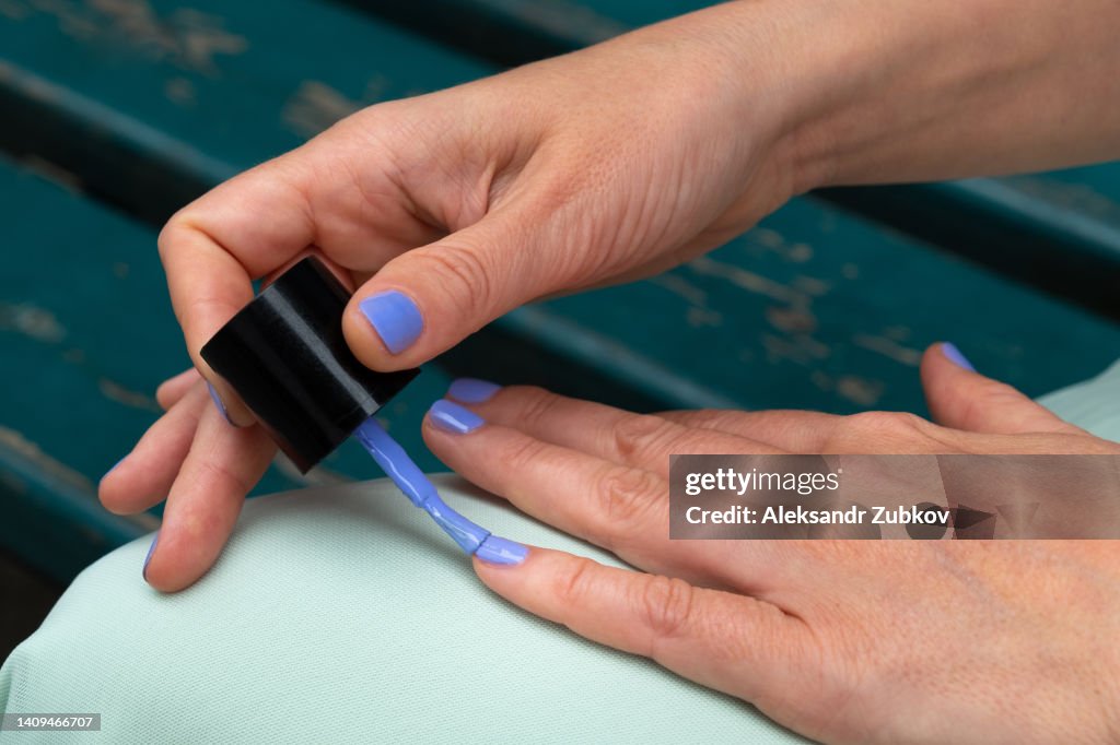 A high school student does a manicure. A woman paints her nails with nail polish in a bright color. An independent manicure in the open air, and not from a cosmetologist. Do it yourself. Body care during your stay at home, during closed beauty salons.