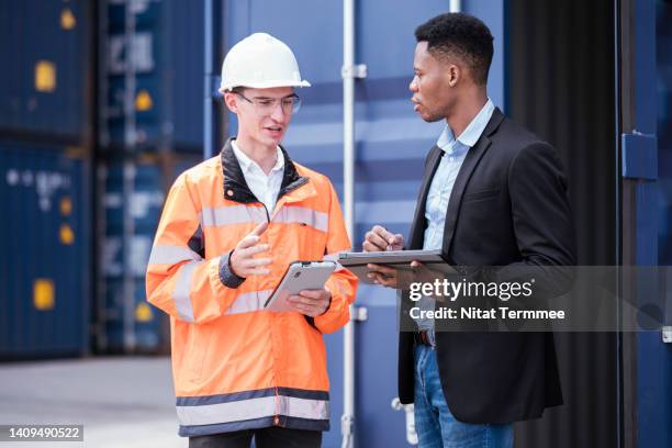 freight forwarder and customs clearance service. an african american shipper discussing with a customs officer in front of a container during loading or customs clearance in a shipping port. - marine engineering stock pictures, royalty-free photos & images