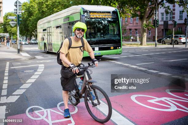 ciclista masculino parado em uma ciclovia no centro da cidade. algum tráfego irreconhecível em segundo plano. - single lane road - fotografias e filmes do acervo