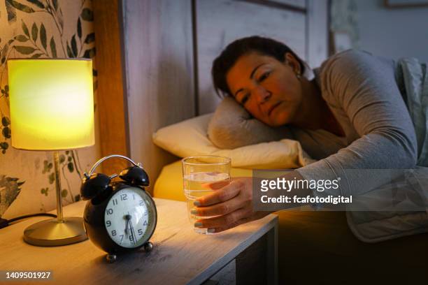 woman in bed reaching glass of water early morning - mature woman in water stock pictures, royalty-free photos & images