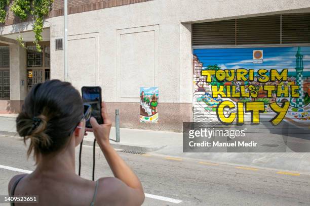 Tourist takes a photo of a graffiti against tourism on July 18, 2022 in Barcelona, Spain. In 2019, 12 million tourists visited Barcelona. Now in...