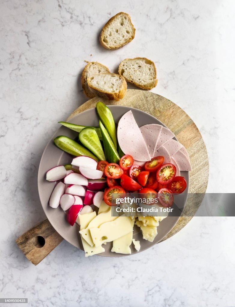 Appetizer plate with vegetables, deli meat and cheese on wooden cutting board on white background
