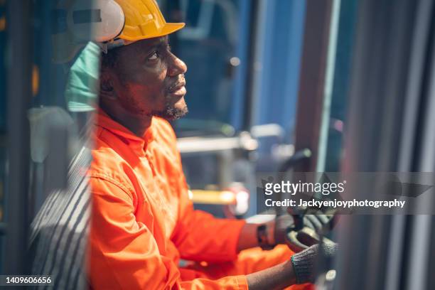african american male cargo handler operating industrial crane at shipping yard - dock worker stockfoto's en -beelden