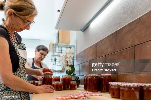 senior mother and mature daughter in domestic kitchen canning in jars traditional homemade apricot jam - canning stock pictures, royalty-free photos & images