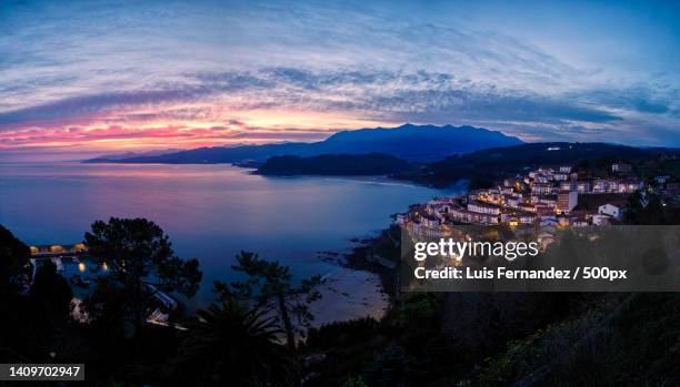 high angle view of illuminated buildings by sea against sky at sunset,lastres,asturias,spain - lastres stock pictures, royalty-free photos & images