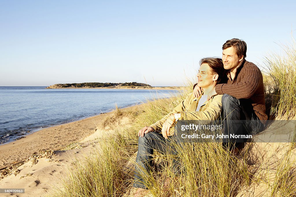 Male gay couple sitting together in sand dunes
