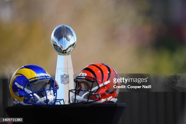 The Vince Lombardi Trophy sits on a table next to Los Angeles Rams and Cincinnati Bengals helmets at a press conference prior to Super Bowl LVI at...