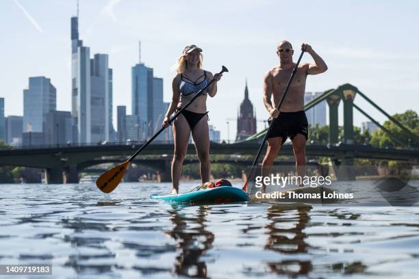Tourist couple paddles boards on the river Main in front of the Skyline in air temperatures of 38 degrees Celcius on July 19, 2022 in Frankfurt,...