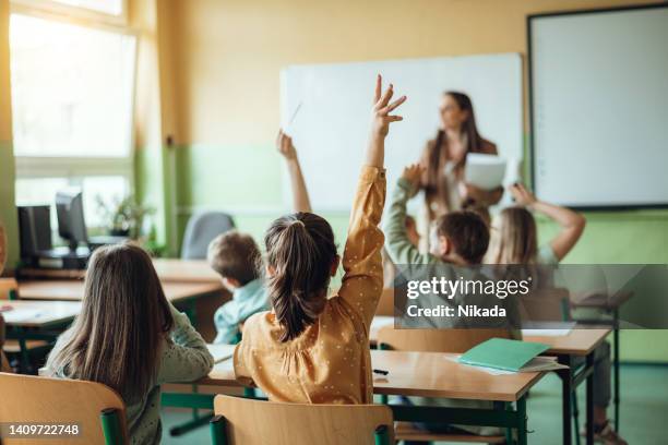 élèves levant la main pendant que l’enseignant leur pose des questions en classe - école photos et images de collection