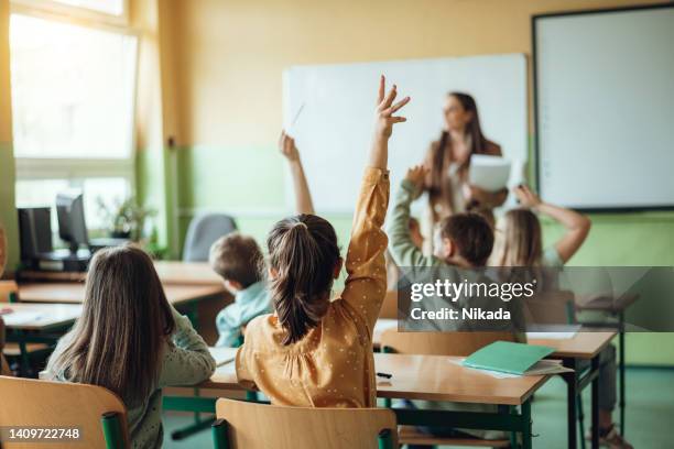 students raising hands while teacher asking them questions in classroom - studeren stockfoto's en -beelden