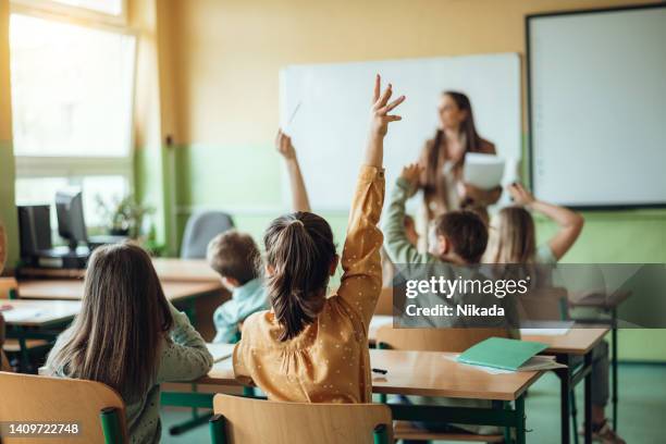 students raising hands while teacher asking them questions in classroom - children bildbanksfoton och bilder