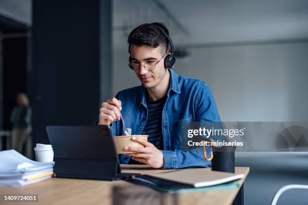 university student studying online on his digital tablet while having lunch in the library - lunch and learn stock pictures, royalty-free photos & images