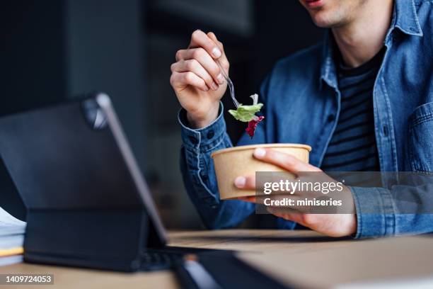 an anonymous student studying online on his digital tablet and eating lunch in the library - take out food imagens e fotografias de stock