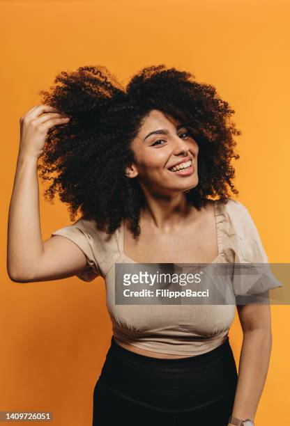 young adult smiling woman against an orange yellow background is fixing her hair - combing stock pictures, royalty-free photos & images