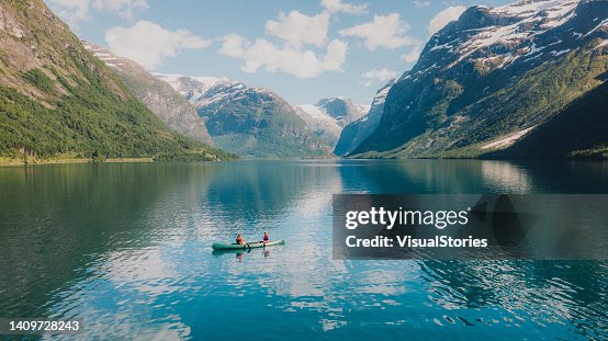Vista aérea de mulher e homem contemplando o verão na Noruega canoagem no lago Lovatnet Vista aérea de mulher e homem contemplando o verão na Noruega canoagem no lago Lovatnet