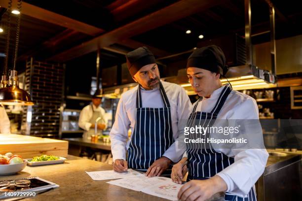 equipe de cozinheiros trabalhando em um restaurante e discutindo o menu - uniforme de cozinheiro - fotografias e filmes do acervo