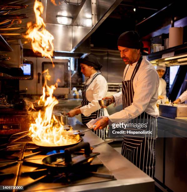 chef cooking at a restaurant and flaming the food - restaurant kitchen stock pictures, royalty-free photos & images