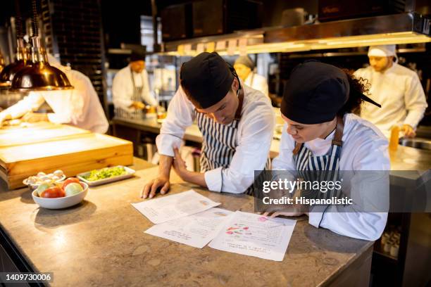 equipo de cocineros que trabajan en un restaurante y miran una receta - protocolo fotografías e imágenes de stock