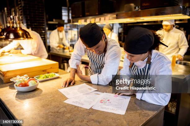 team of cooks working at a restaurant and looking at a recipe - restaurant manager stock pictures, royalty-free photos & images