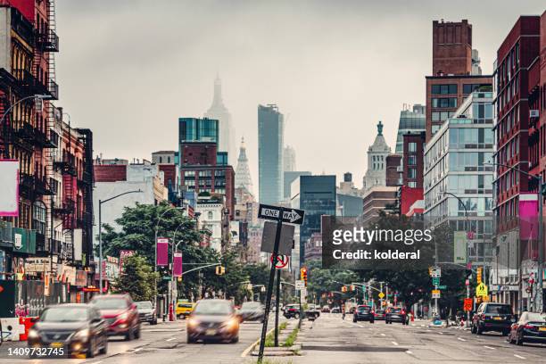 soho district streets with car blurred motion, brick row houses and distant foggy view of empire state building - soho manhattan stockfoto's en -beelden
