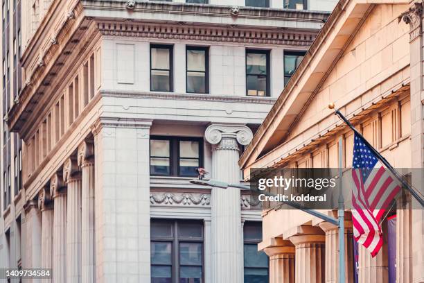 neoclassical architecture of lower manhattan, wall street buildings with american flag flying - historic stock exchange building stock pictures, royalty-free photos & images