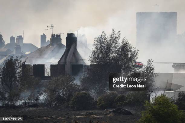 Union Flag flies amongst the smouldering ruins of houses as fire services tackle a large blaze on July 19, 2022 in Wennington, England. A series of...