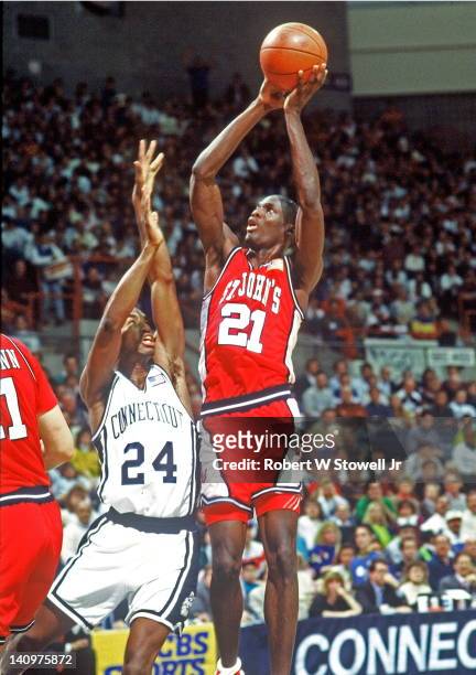 American basketball player Malik Sealy, of St. John's University, shoots a jumpshot over the outstretched arms of guard Scott Burrell, of the...
