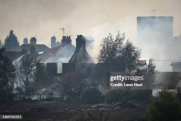 Union Flag flies amongst the smouldering ruins of houses as fire services tackle a large blaze on July 19, 2022 in Wennington, England. A series of...