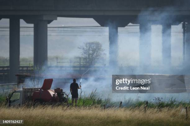 Man attempts to damp down the smouldering field with a hose pipe as fire services tackle a large blaze on July 19, 2022 in Wennington, England. A...