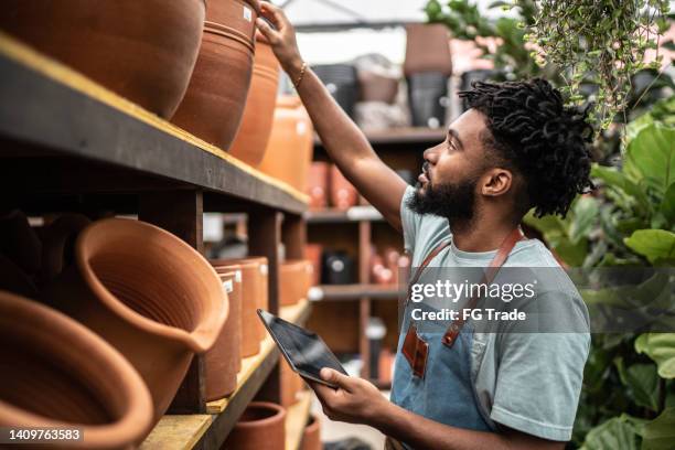 young salesman working on a digital tablet at a garden center - shop seller stock pictures, royalty-free photos & images