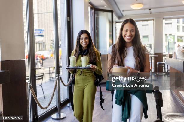 two women friends walking in a cafe carrying their food and drinks - mittagspause stock-fotos und bilder